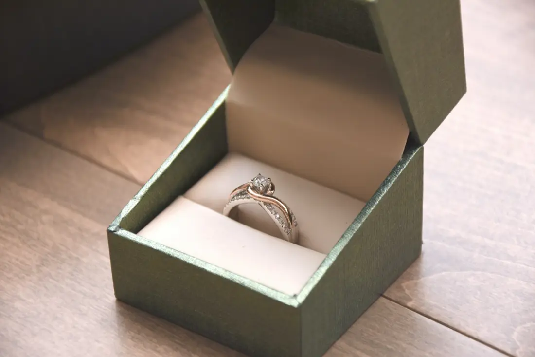 Estuche de regalo verde abierto con un anillo de piedra apoyado en su almohadilla.