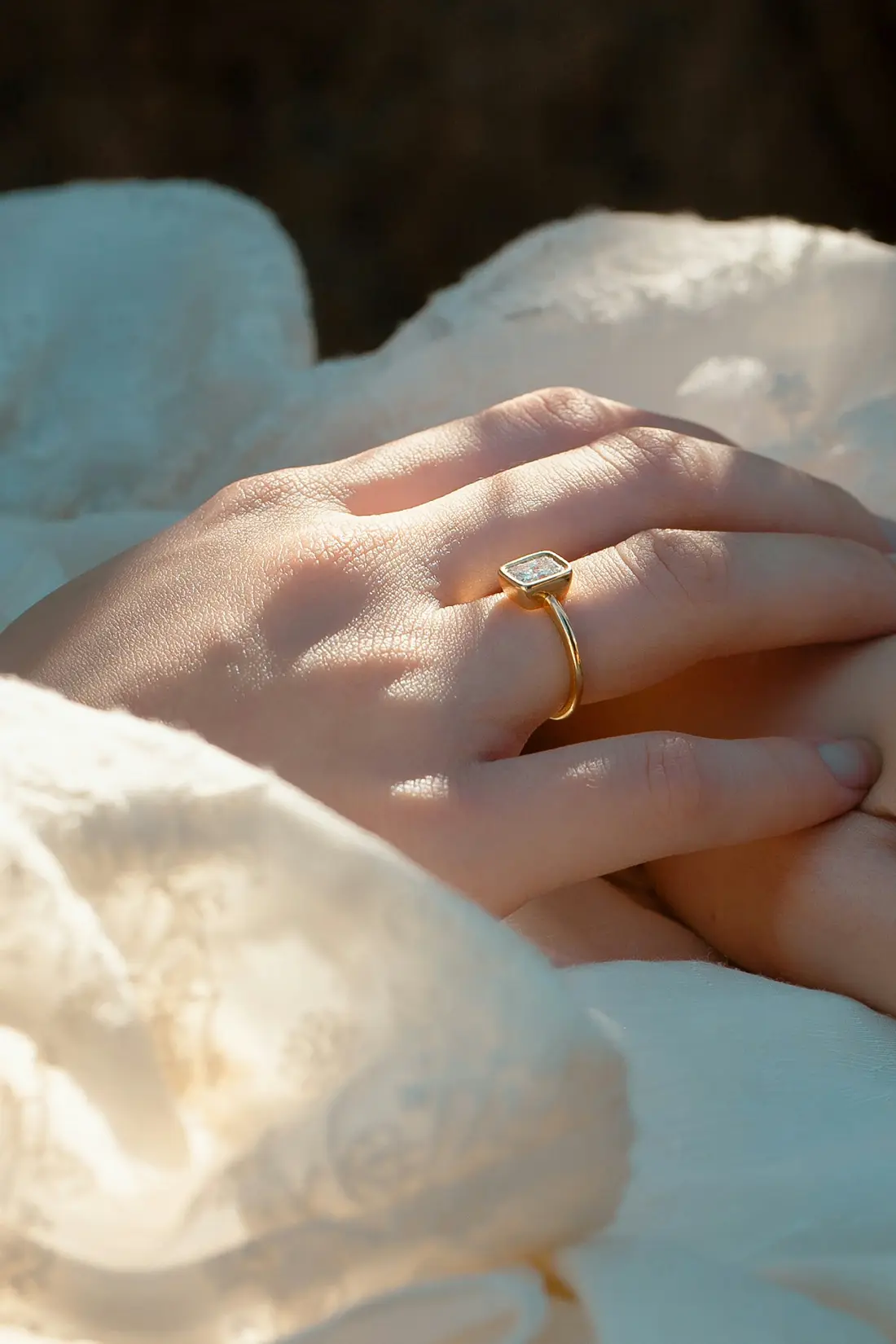 Mano apoyada sobre una tela clara con un anillo dorado de piedra en el dedo, bajo luz cálida.